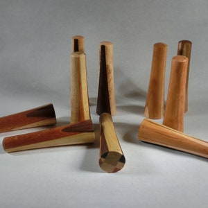 May include: A selection of wooden bottle stoppers in different shapes and wood grains. Some are cylindrical, others are conical. The colours vary from light tan to dark brown, displaying the natural wood patterns. The stoppers are arranged on a neutral background.