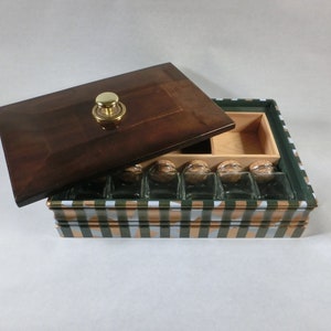 May include: A wooden box with a dark brown lid and a gold knob. The box has a green, white, and gold plaid pattern. Inside are several small glass bottles with cork stoppers.