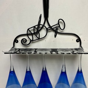 May include: A black metal wine glass rack holding five blue-bowled wine glasses. The rack has a decorative design with swirls and loops. The wine glasses are suspended upside down, showcasing their vibrant blue color.