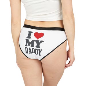Pode incluir: Cuecas brancas com acabamento preto e o texto "I ❤️ MY DADDY" em preto e vermelho. A roupa interior tem uma cintura preta e uma borda preta nas bordas.