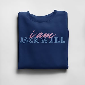 May include: A navy blue sweatshirt with the text "i am JACK & JILL" in pink and light blue. The sweatshirt is folded neatly on a white surface. The text is in a script font.