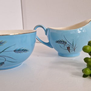 May include: A blue and white sugar bowl and creamer set with a wheat design. The set is made of ceramic and has a gold rim.