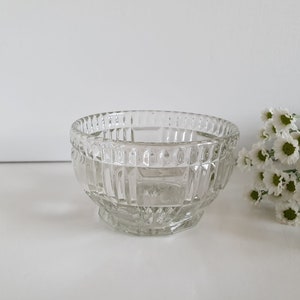 Könnte beinhalten: Eine klare Glasschüssel mit einem dekorativen, geometrischen Muster. Die Schüssel ist leer und steht auf einer weißen Oberfläche.