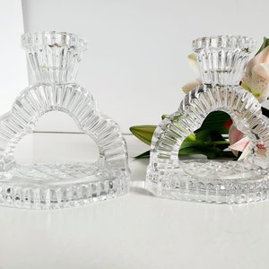 May include: Two clear glass candle holders shaped like hearts with a raised design. The candle holders have a small, round opening at the top for a candle.