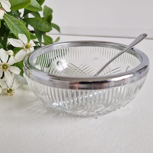 Könnte beinhalten: Eine klare Glasschüssel mit silbernem Rand und einem kleinen Löffel im Inneren. Die Schüssel hat ein Diamantenmuster auf dem Boden und steht auf einer weißen Oberfläche.