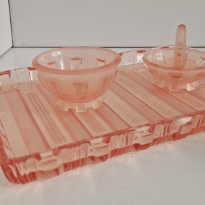 Puede incluir: Un juego de tocador de cristal rosa vintage. El juego incluye una bandeja rectangular con diseño acanalado, un cuenco pequeño y un portaanillos. La bandeja mide unos 20 cm de largo.