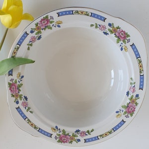 May include: A white ceramic bowl with a blue and yellow floral pattern around the rim. The bowl is empty and has a slight sheen.