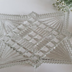 May include: A clear glass serving tray with a starburst design. The tray has a raised, geometric pattern and a scalloped edge.