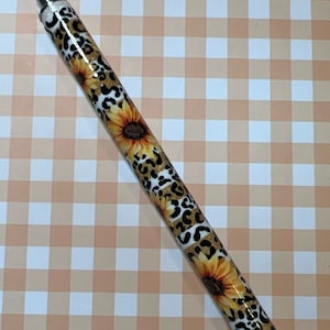 May include: A silver pen with a white and brown leopard print design and yellow sunflowers.