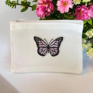 May include: A white canvas zippered pouch with a pink butterfly embroidered on the front.