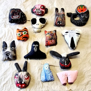 May include: A collection of 13 handmade plush toys, each with a unique design and personality. The toys are made from a variety of fabrics and materials, including felt, cotton, and embroidery thread. The toys are all different shapes and sizes, and they are all very colorful.