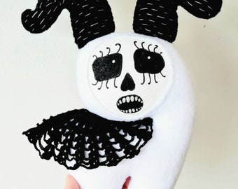 May include: White plush toy with a black skull face, long black ears, and a black lace collar. The toy has a stitched-on smile and large black eyes.