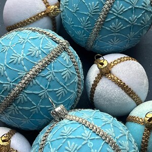 Könnte beinhalten: Ein Set aus sechs blauen und weißen Weihnachtskugeln mit einem zarten Schneeflockenmuster und goldenen Verzierungen.