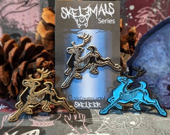 Pode incluir: Dois pinos de esmalte com renas esqueléticas em ouro e azul. Os pinos fazem parte da "Skelanimals Series" e são etiquetados como "Skeleer" por VicCreates.art.