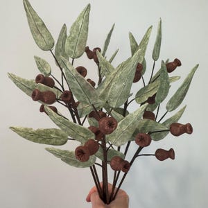 May include: A bunch of artificial eucalyptus stems with brown seed pods. The stems are green with a textured, slightly fuzzy finish.