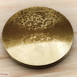 Peut inclure: Un compact doré avec un motif floral. Le compact est rond et a un couvercle à charnière.
