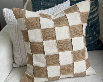 May include: A brown and white checkered throw pillow with a burlap texture. The pillow is sitting on a white couch.