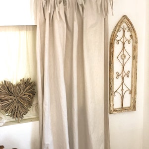 May include: A pair of off-white linen curtains with a simple tie-top design. The curtains are hung on a black metal rod and are gathered at the top.