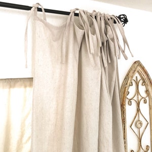 May include: A pair of off-white linen curtains with a black curtain rod. The curtains are tied back with fabric ties.