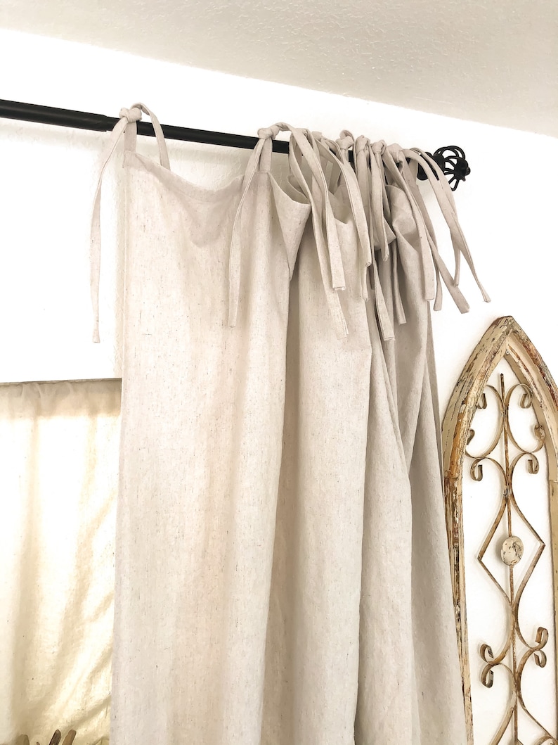 May include: A pair of off-white linen curtains with a black curtain rod. The curtains are tied back with fabric ties.