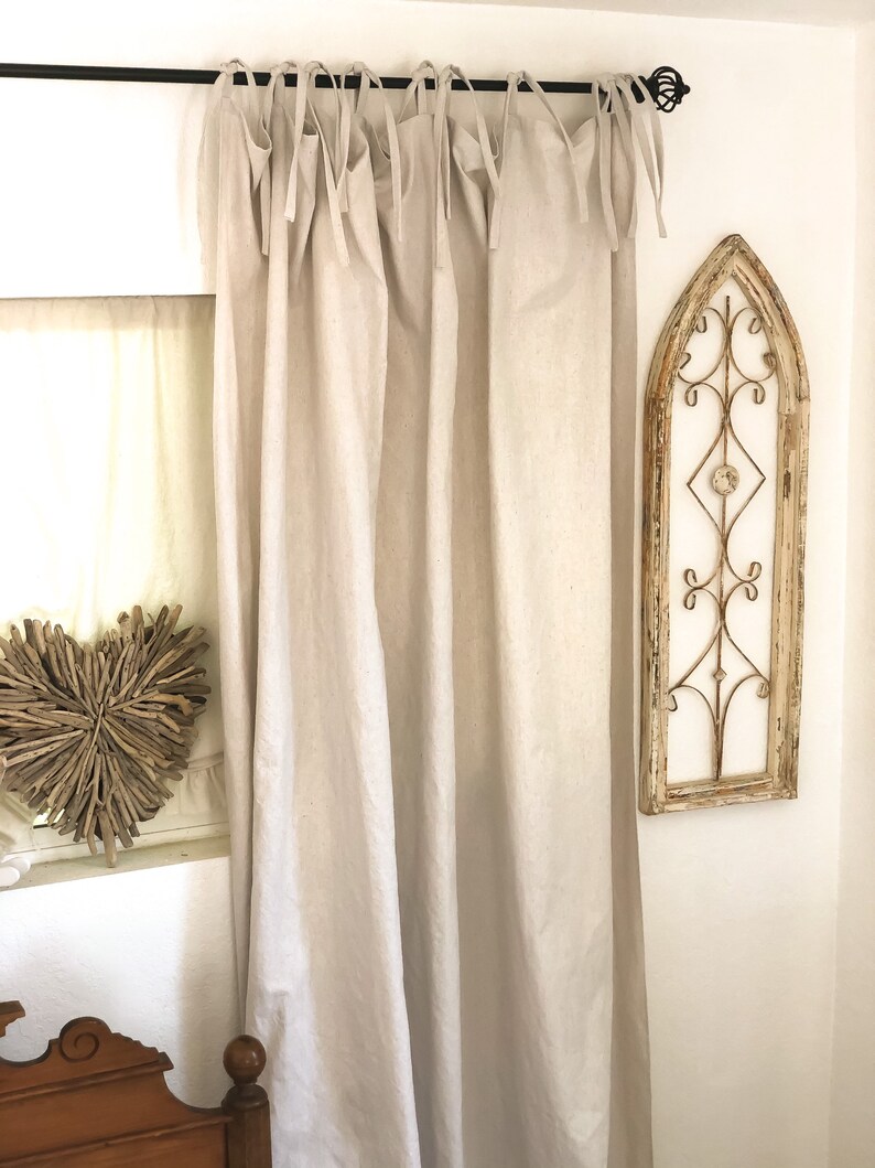May include: A pair of off-white linen curtains with a simple tie-top design. The curtains are hung on a black metal rod and are gathered at the top.