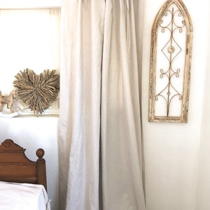 May include: A pair of off-white linen curtains with a simple tie-top design. The curtains are hanging from a black metal rod and are gathered at the top.