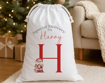 Puede incluir: Bolsa de regalo navideña blanca con cierre de cordón. La bolsa presenta el texto "Special Delivery For Harry" en gris y rojo, junto con una gran letra "H" roja y una ilustración de Papá Noel.