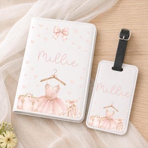 May include: White passport holder and luggage tag set with a ballet theme. The set features a pink tutu, suitcase, and the name "Millie" in pink script. A black strap with a silver buckle is attached to the luggage tag.