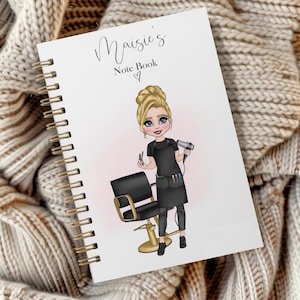 May include: White spiral-bound notebook with the text "Maisie's Note Book" and a heart. The cover features an illustration of a blonde-haired hairstylist holding scissors and a hairdryer, with a salon chair in the background.
