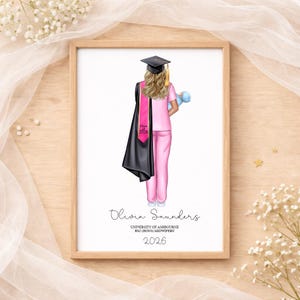 May include: A framed print depicting a graduate in pink scrubs, a black graduation gown, and a pink sash with "Class 2026." The graduate holds a blue baby doll. The print includes the name "Olivia Saunders" and "University of Ashbourne BSc (Hons) Midwifery 2026."