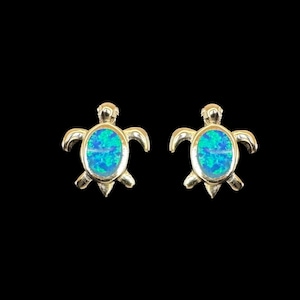 Könnte beinhalten: Ein Paar silberne Schildkrötenohrringe mit blauen Opal-Edelsteinen. Die Schildkröten sind nach vorne gerichtet, mit erhobenem Kopf und ausgestreckten Beinen.