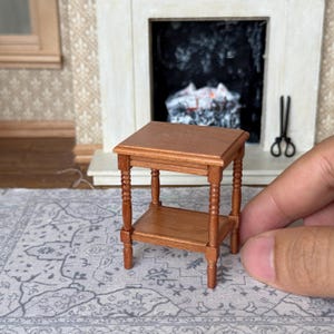 Puede incluir: Mesa auxiliar de madera en miniatura, color marrón cálido. Cuenta con una superficie cuadrada, una balda inferior y cuatro patas torneadas. Aproximadamente 7.6 cm de altura, ideal para casas de muñecas.