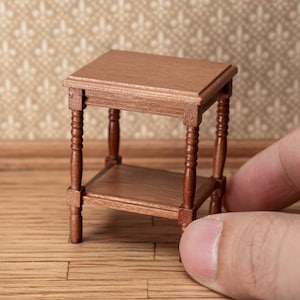 May include: Miniature wooden side table with a rectangular top and a lower shelf. The table has four turned legs and is finished in a warm brown stain. The table measures approximately 2.5 inches in height and 2 inches in width.