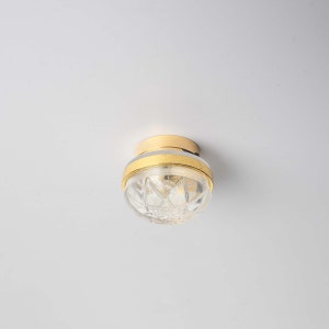 Op de afbeelding: Een gouden plafondlamp met een heldere glazen kap met een diamantpatroon.