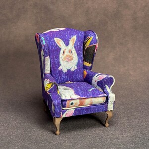 May include: A miniature wingback chair upholstered in a vibrant purple fabric featuring a repeating pattern of white and tan rabbits. The small furniture piece has curved wooden legs and a structured backrest with side wings and padded armrests.