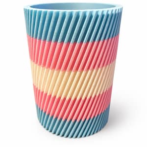 May include: A cylindrical container with a ridged exterior, 3D-printed in blue, pink, and cream bands. The top rim is light blue. The design suggests a decorative or functional item, possibly for storage or display.