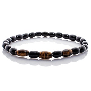 Op de afbeelding: Een zwarte en bruine kralen armband met ovale kralen. De armband heeft een patroon van afwisselende zwarte en bruine kralen.