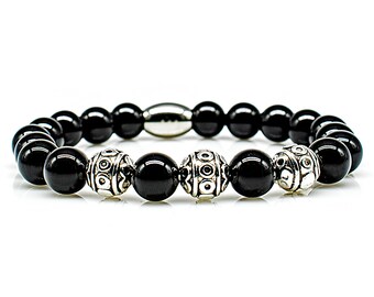 Op de afbeelding: Een armband van zwarte onyx kralen met zilveren accenten. De armband heeft een zilveren sluiting en drie zilveren kralen met ingewikkelde ontwerpen.
