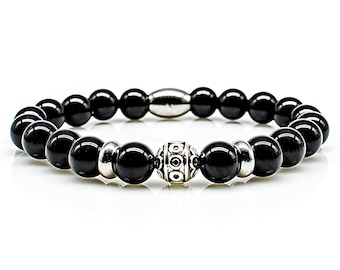 Op de afbeelding: Zwarte kralen armband met een zilveren bedel. De armband is gemaakt van ronde zwarte kralen en heeft een zilveren bedel met een decoratief ontwerp.