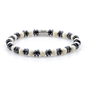 Op de afbeelding: Een kralenarmband met witte, ronde kralen afgewisseld met zwarte, schijfvormige kralen en zwarte, cilindrische kralen. De armband heeft een zilverkleurige sluiting. De lengte is ongeveer 18 cm.