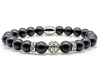 Op de afbeelding: Een zwarte kralen armband met een zilveren bedel en twee zilveren accenten met heldere stenen.