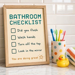 May include: A framed bathroom checklist with the text "BATHROOM CHECKLIST" in teal pixelated font. The checklist includes prompts like "Did you flush" and "Wash hands." A polka-dot toothbrush holder with toothbrushes, a rubber duck, and a striped towel are nearby.