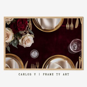Könnte beinhalten: Gerahmtes Bild einer formellen Tischdekoration. Goldgeränderte Teller mit gefalteten Servietten, goldenem Besteck und klaren Gläsern sind auf einer tiefroten Tischdecke angeordnet. Ein Strauß Rosen in Creme und Burgunderrot sorgt für einen Hauch von Eleganz. Der Text "CARLOS V | FRAME TV ART" steht unten.