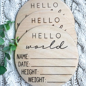 May include: A set of three round wooden signs with the text "Hello World" and blank lines for name, date, height, and weight. The signs are stacked on top of each other.
