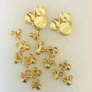 May include: Gold-tone dangle earrings featuring a Mickey Mouse head design. The earrings are made of metal and have a dangling chain of Mickey Mouse heads. The back of the earrings have the text "Disney" and "&copy;Disney" on them.