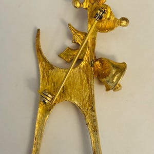 May include: Gold-toned metal Christmas reindeer brooch with a bell and a bow. The brooch has a pin back.