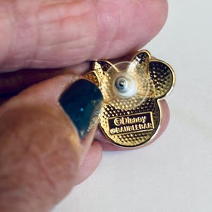 May include: Gold-colored Mickey Mouse pin with a clear plastic backing. The back of the pin has the text "&copy;Disney  &copy;AUBLEEBAR".