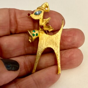 May include: Gold-tone reindeer brooch with red, blue, and green rhinestones. The reindeer is wearing a Santa hat and has a bell around its neck.