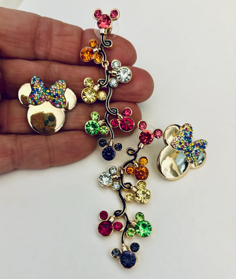 May include: A pair of gold-tone dangle earrings featuring a cluster of colorful crystal Mickey Mouse heads. The earrings are designed with a dangling chain of Mickey Mouse heads with different colored crystals. The earrings are perfect for adding a touch of Disney magic to any outfit.