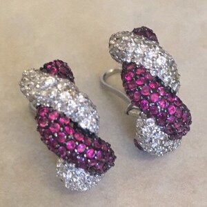 May include: A pair of silver earrings with a twisted design. The earrings are set with small, sparkling white diamonds and pink rubies.